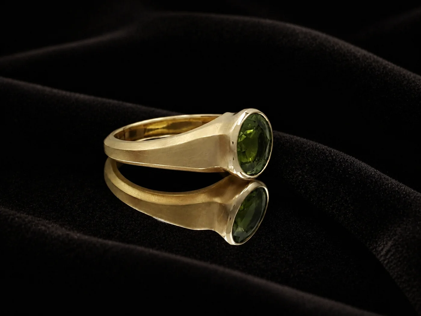 Goldring mit grünem facettiertem Edelstein auf schwarzem Samt