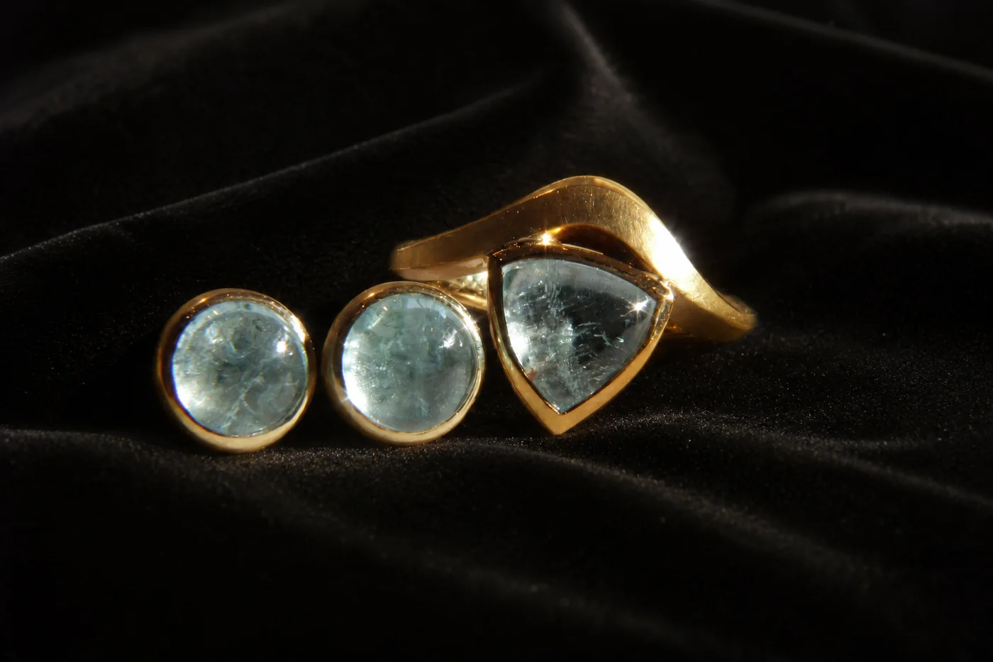 Goldring und Ohrstecker mit hellblauen Edelsteinen auf schwarzem Samt